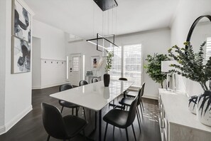 Une cuisine moderne avec un comptoir blanc, des chaises noires et un luminaire suspendu.