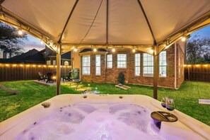 Un bain à remous installé sous une tente, avec une maison en briques en arrière-plan.