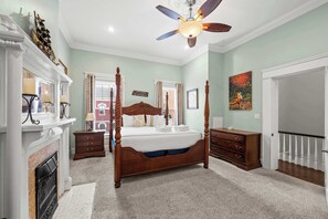 A four-poster bed with a ceiling fan, a fireplace, and a painting on the wall.