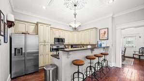 A kitchen with light-colored cabinets, stainless steel appliances, a central island with stools, and a chandelier. - Game Room, Back Yard, Close to Stadiums & Downtown (Covington)