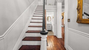 A staircase with white walls and wooden steps leading to a room with a mirror and a clock. - Game Room, Back Yard, Close to Stadiums & Downtown (Covington)