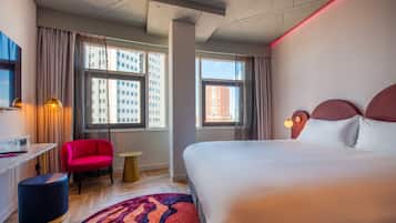 Ein Hotelzimmer mit einem großen Bett, einem Schreibtisch, einem Stuhl und einem kleinen runden Tisch.