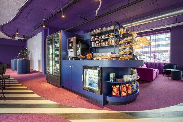 A purple-themed bar area with a refrigerator, shelves stocked with snacks, and a seating area with a purple couch and chairs. - Hotel VIC (Leiden)