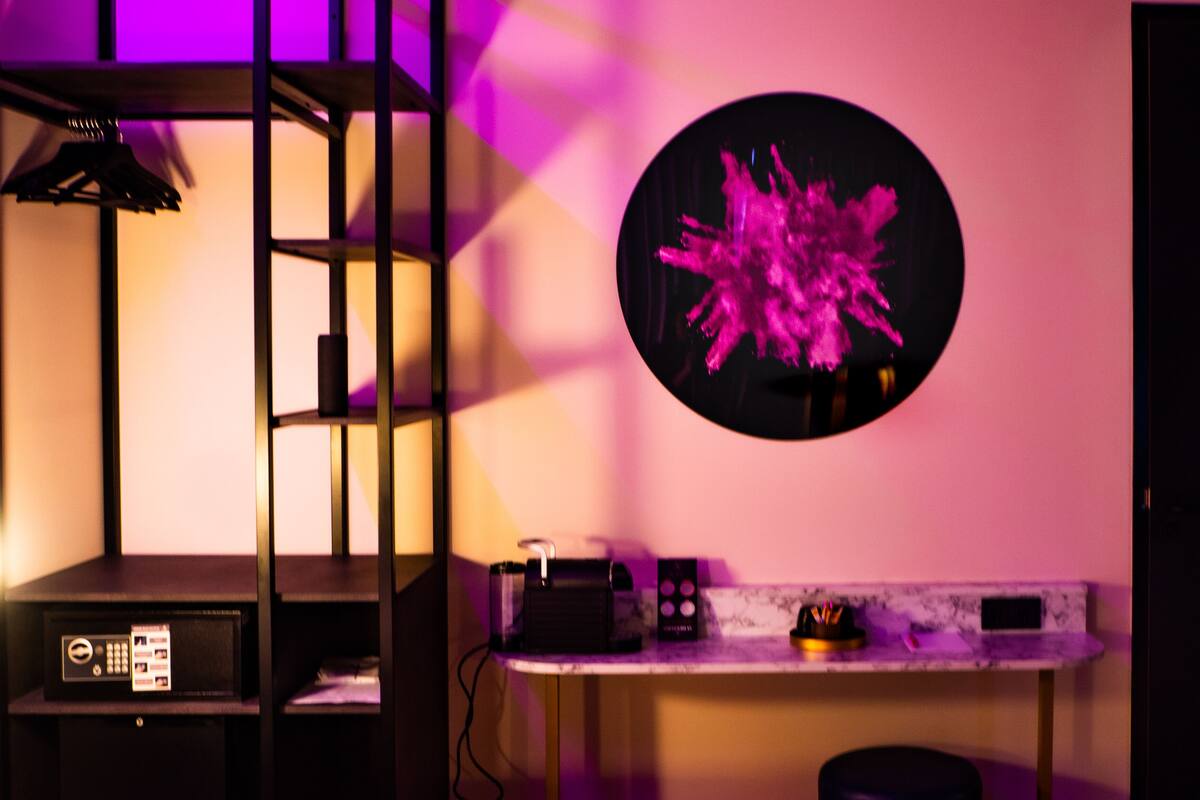 A room with a bunk bed, a desk with a computer, a coffee machine, and a wall-mounted circular artwork.