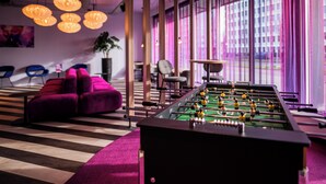 Un espacio interior moderno con mesa de fútbol, asientos morados y ventanas grandes con cortinas.