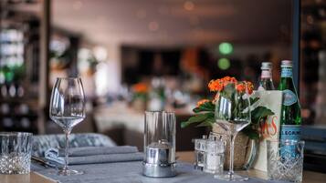 Een gedekte tafel met glazen, een flesje San Pellegrino water en een vaas met oranje bloemen.