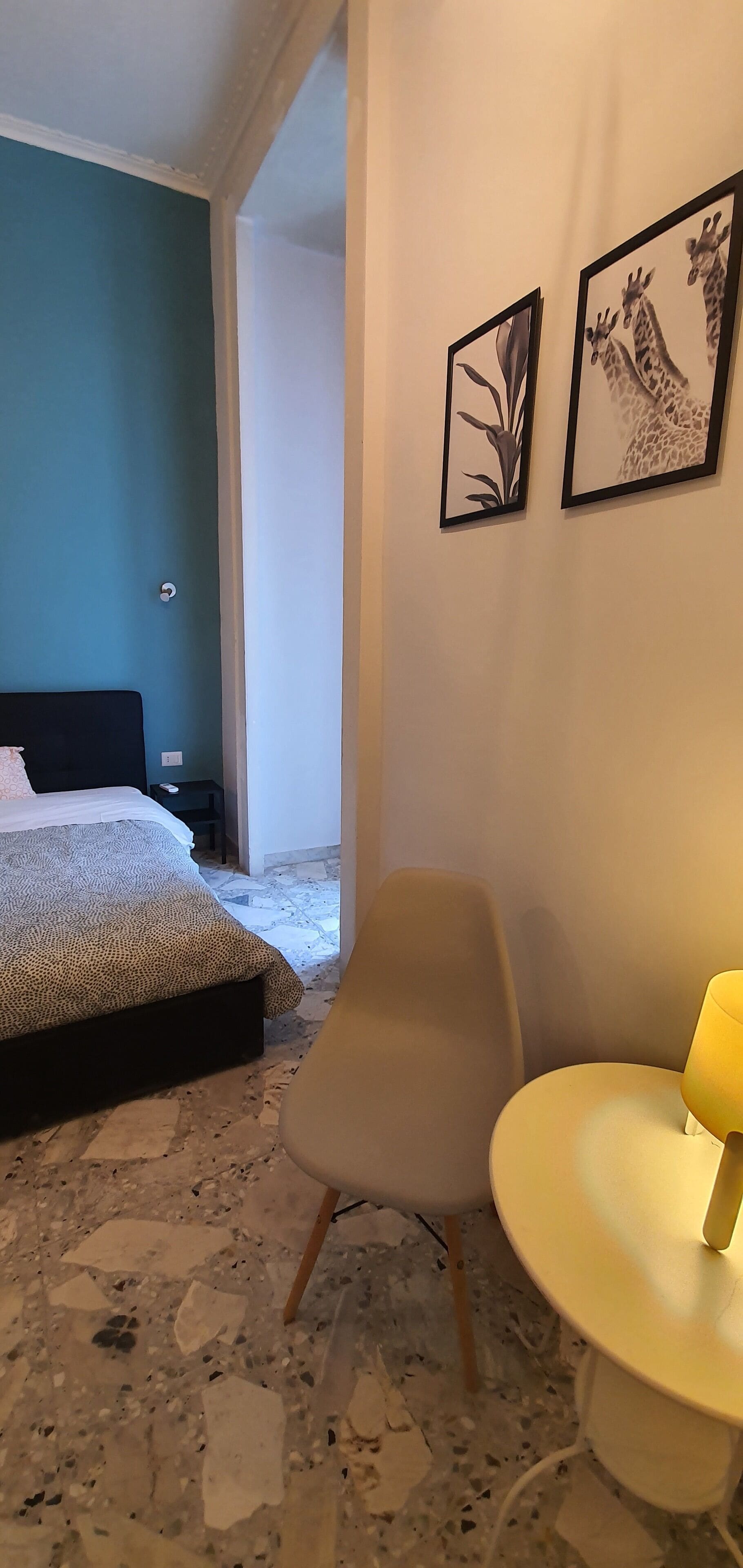 Une chambre à coucher avec un lit, une chaise, une table et deux tableaux encadrés accrochés au mur.