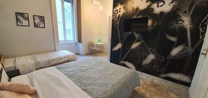 Une chambre à coucher comprenant un lit, une table de chevet, une petite table avec une chaise, et un mur orné d’une fresque florale.