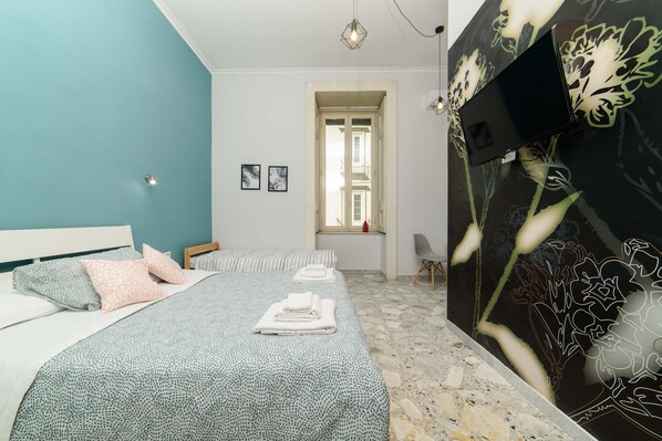 Une chambre à coucher avec un lit, des oreillers, un téléviseur à écran plat, une fenêtre et une porte.