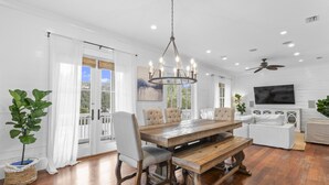 A spacious dining area with a wooden table and chairs, a chandelier, and a large TV mounted on the wall.