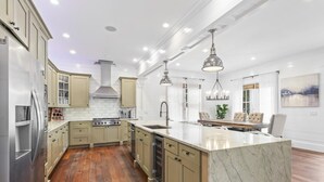 A modern kitchen with wooden cabinets, a marble island, stainless steel appliances, and pendant lighting.