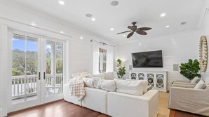 A spacious living room with a white sofa, a television mounted on the wall, and a ceiling fan.