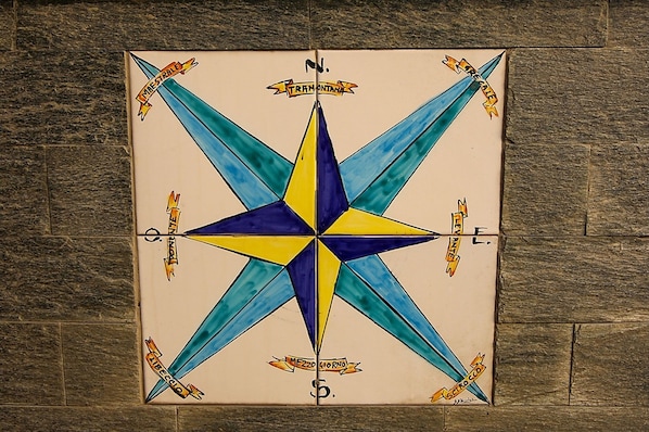 Um azulejo com design de bússola, contendo indicações de direção e a palavra 'TRAMONTANA' na parte superior.