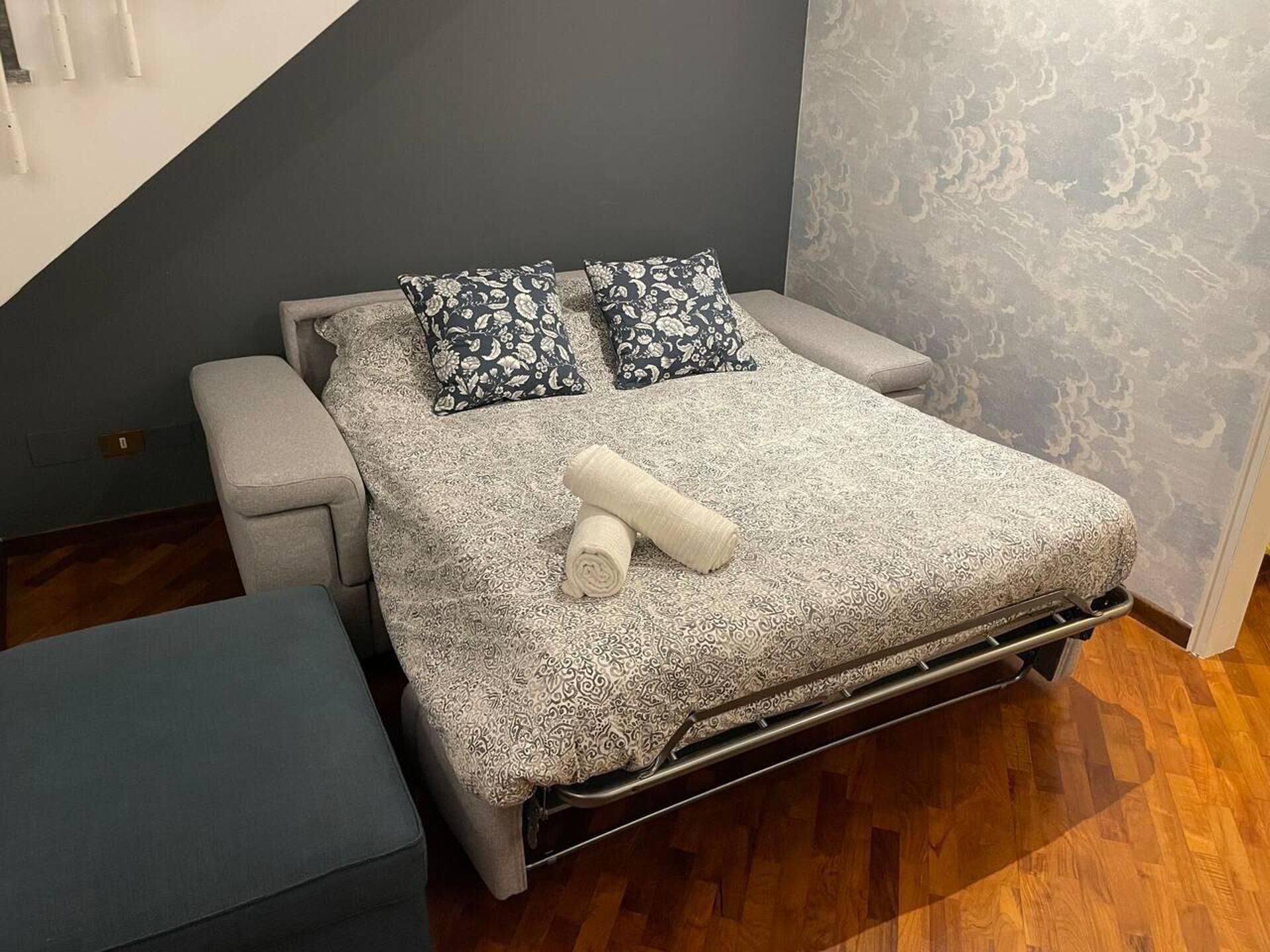 A modern bedroom with a bed, two pillows, a rolled towel, and a small bench.