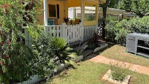 Una casa petita amb un porxo, envoltada per una valla blanca de palets i diverses plantes.