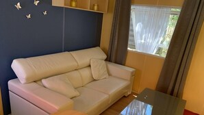 Una habitació amb un sofà beix, una taula de fusta i una taula amb sobre de vidre.