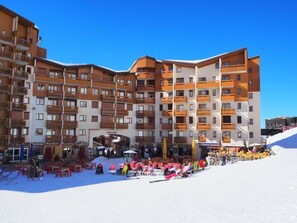 A multi-story hotel with balconies, outdoor seating, and a ski slope in the background.