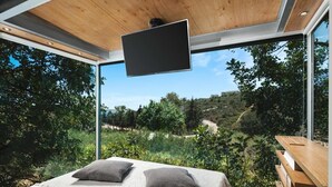 Een slaapkamer met een groot bed, twee kussens, een houten hoofdbord en een aan het plafond bevestigde televisie.