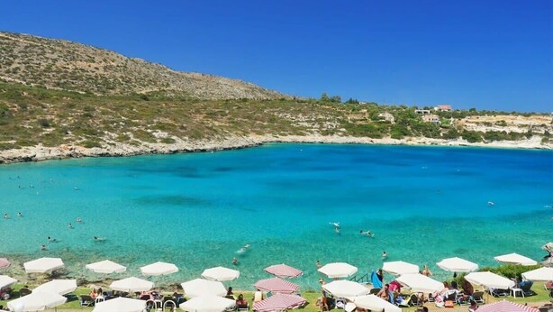 Een kuststrand met helder turquoise water, strandparasols en mensen die zwemmen en ontspannen.