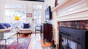 A living room with a fireplace, a television mounted above it, and a large window with a view of trees. - Heart of Capitol Hill Row House, Luxury & Location (Washington)