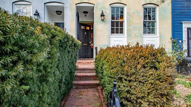 A traditional building with a brick pathway leading to a dark entrance door, surrounded by well-maintained hedges. - Heart of Capitol Hill Row House, Luxury & Location (Washington)