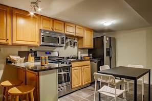A kitchen with wooden cabinets, a microwave, stove, refrigerator, and a dining area with chairs.