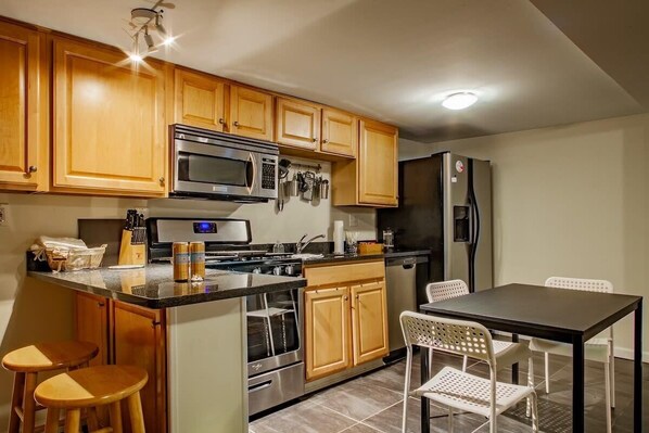 A kitchen with wooden cabinets, a microwave, stove, refrigerator, and a dining area with chairs.