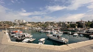 Uma marina com vários barcos atracados, um calçadão à beira-mar e edifícios ao fundo.