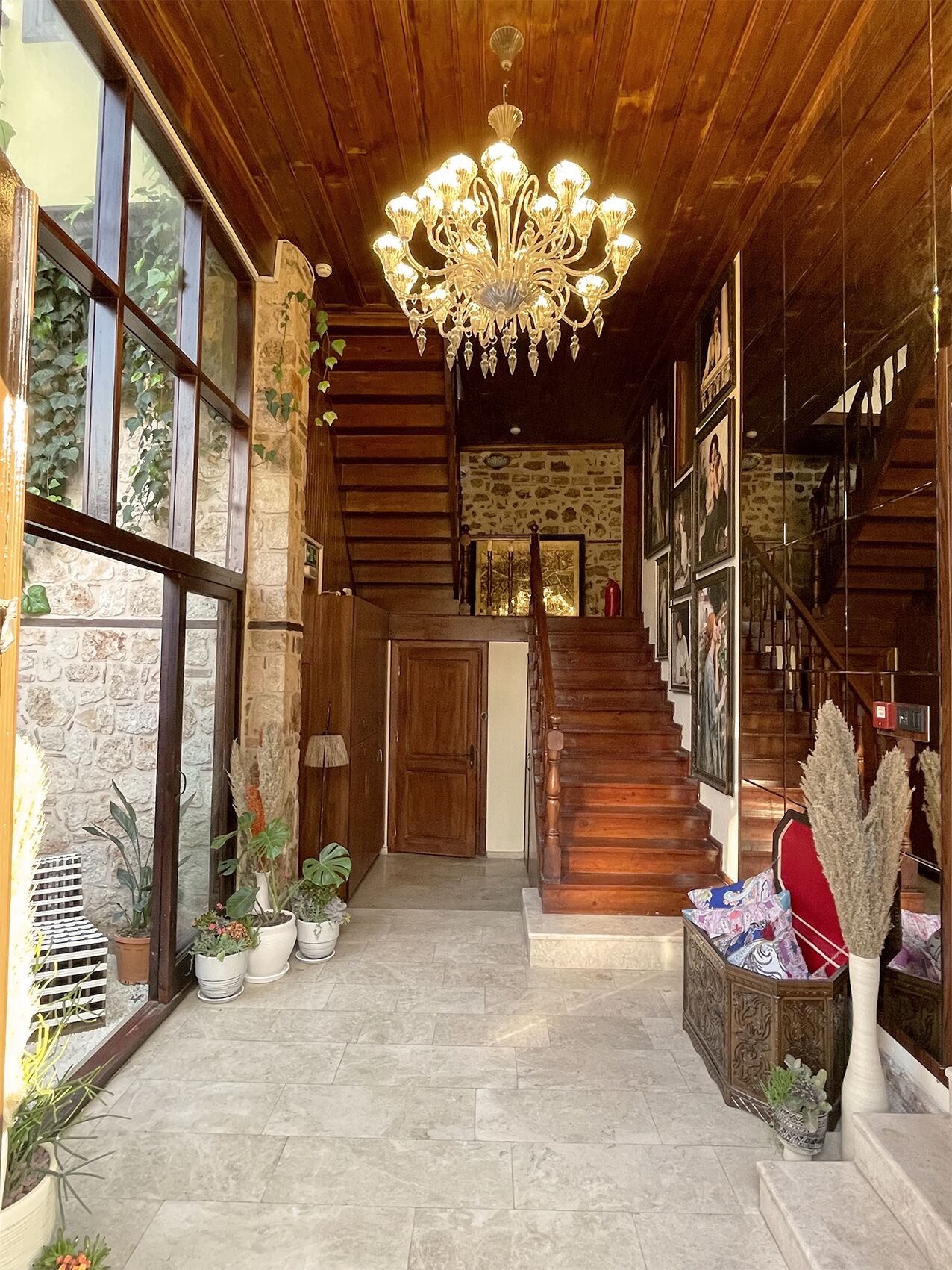 Un amplio pasillo con una escalera de madera, un candelabro y plantas en macetas.