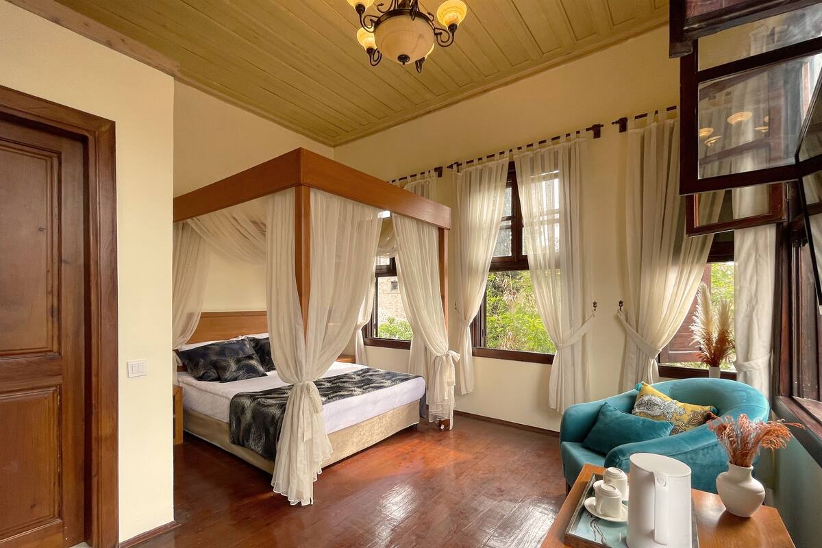 Une chambre à coucher avec un lit à baldaquin, un canapé, une table basse et une vue sur la verdure environnante.