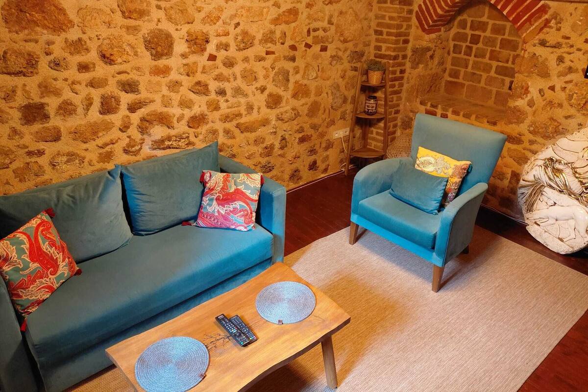 Une pièce avec un mur en pierre, un canapé bleu, un fauteuil bleu, une table basse en bois et un vase blanc décoratif.