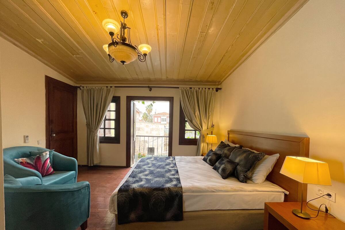 Une chambre d’hôtel avec un lit, une chaise, une table de chevet, une lampe et un ventilateur de plafond.