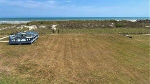Vista de platja amb un vaixell amarrat a l'esquerra i una zona verda en primer pla.
