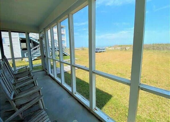 A covered porch with large windows overlooking a grassy field and a building in the distance. - Cool Air Cottage Downstairs OF Duplex (North Myrtle Beach)