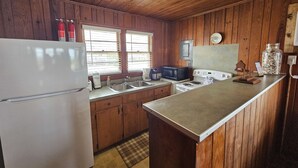 A compact kitchen with wooden walls, a refrigerator, a microwave, a stove, and a sink. - Cool Air Cottage- Upstairs- Ocean Front Duplex (North Myrtle Beach)