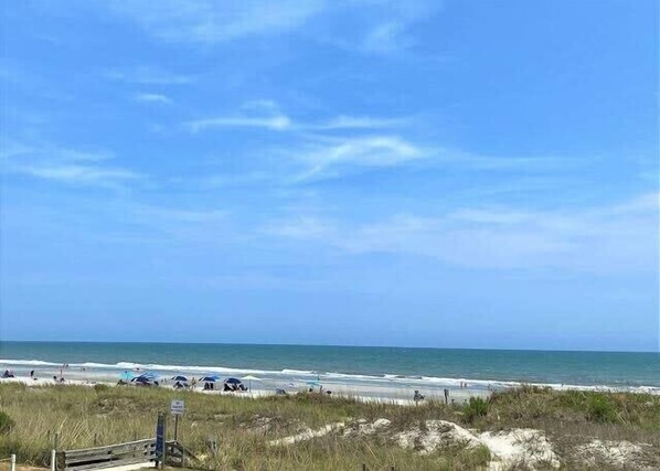 Une plage avec un ciel dégagé, un rivage sablonneux et quelques parasols.