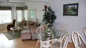 A living room with a glass dining table, white wicker chairs, a sofa, and a coffee table.