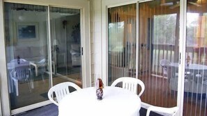 A room with a white table, white chairs, a ceiling fan, and a sliding glass door leading to an outdoor area with a table and chairs.