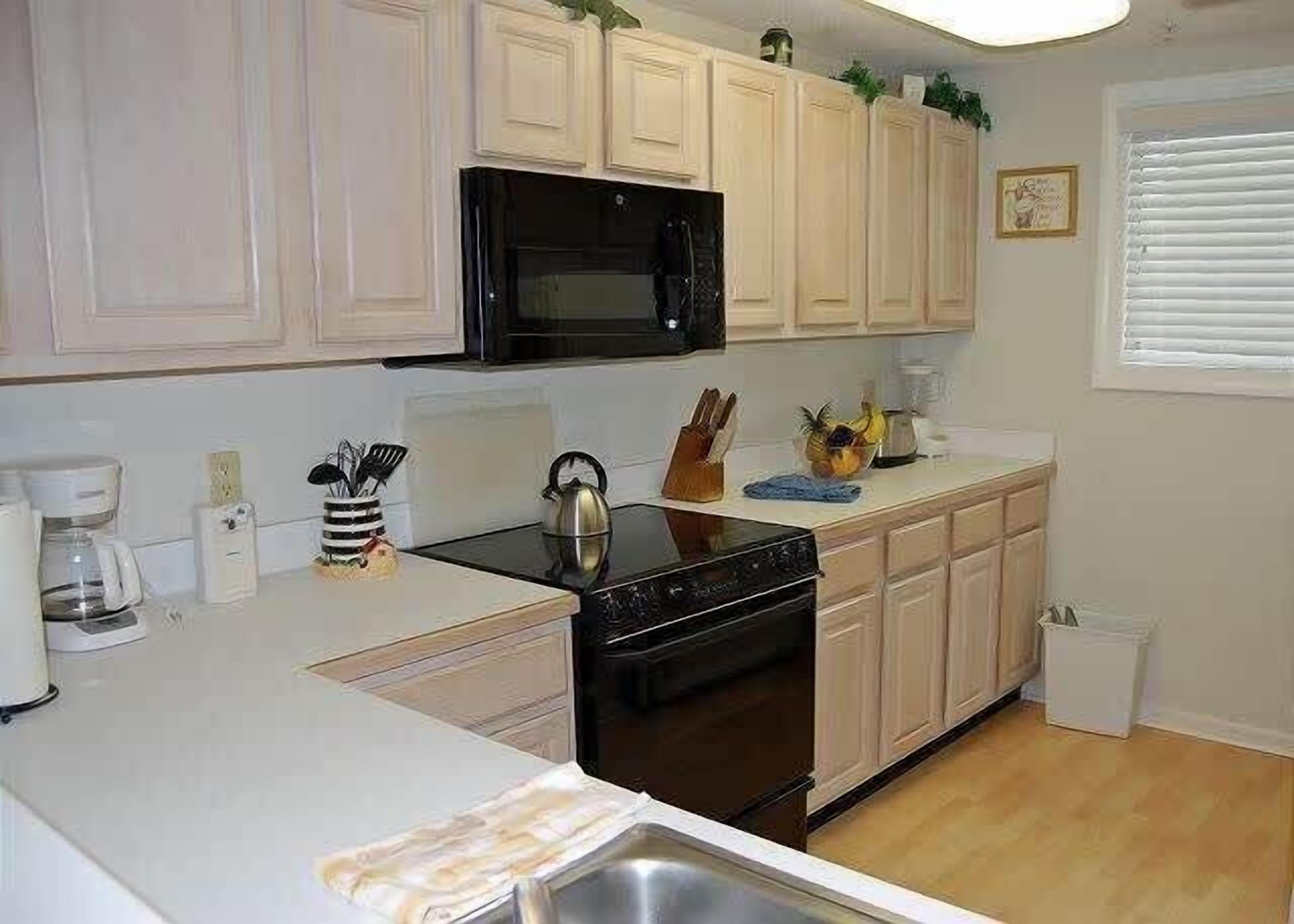 A kitchen with white cabinets, a black microwave, a stove, and a sink.