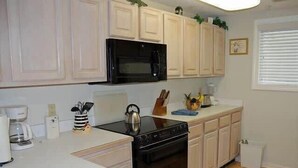 A kitchen with white cabinets, a black microwave, a stove, and a sink.