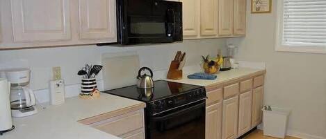 A kitchen with white cabinets, a black microwave, a stove, and a sink.