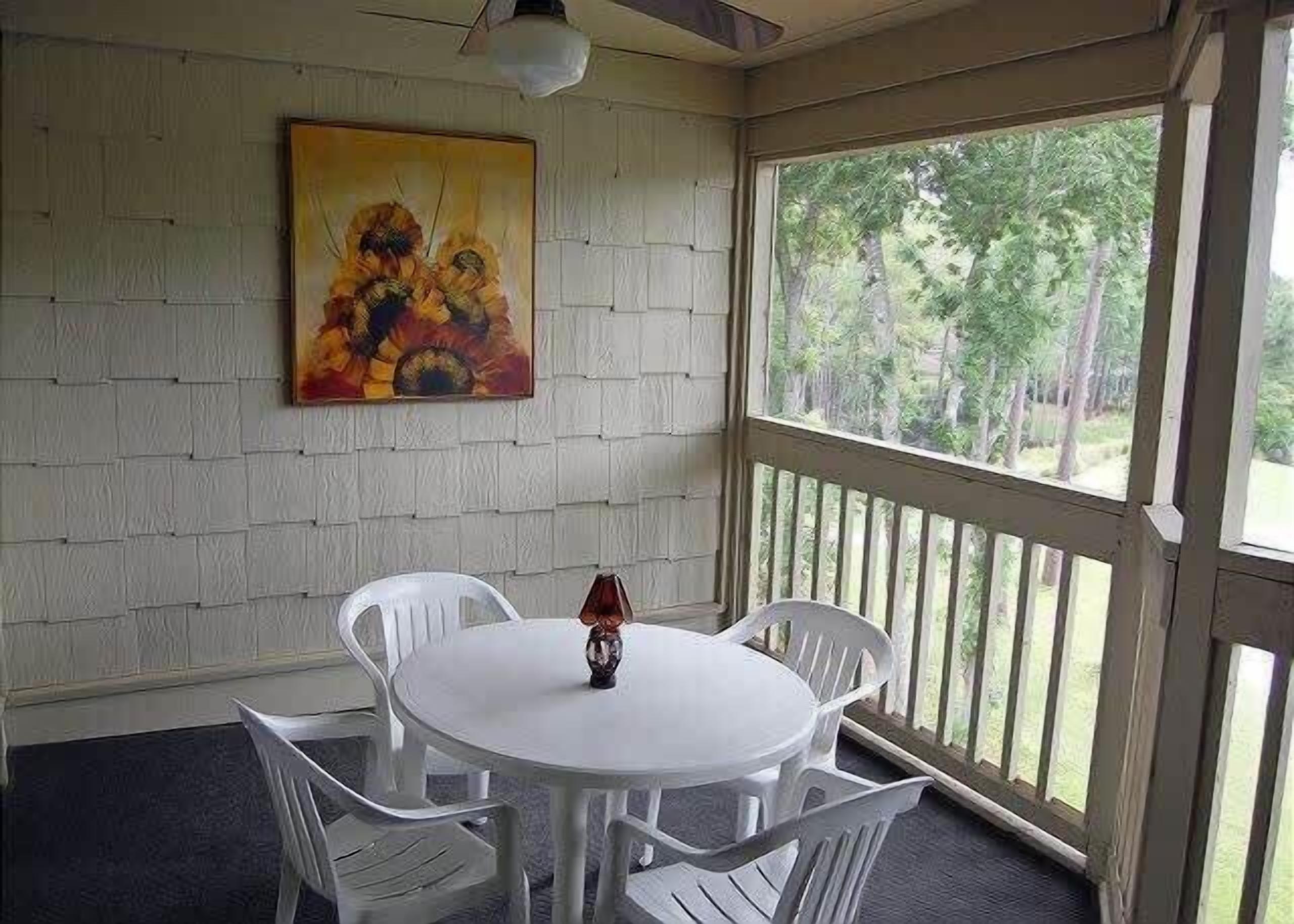 Una habitación con una mesa redonda y cuatro sillas, un cuadro en la pared y vistas a través de un ventanal grande.