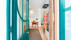 A narrow hallway with teal doors, a wooden floor, a small table with chairs, and a colorful cloth hanging on the wall. - Cozy Apartment in Historical Lisbon by COZYSTAYS 1/5 (Lisbon)