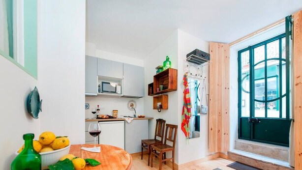 A compact kitchen with a dining area, wooden flooring, and a view through a green door. - Cozy Apartment in Historical Lisbon by COZYSTAYS 1/5 (Lisbon)
