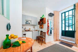 Kompakti keittiö, jossa on ruokailutila, puulattia ja näkymä vihreän oven läpi.