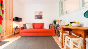 A cozy living room with a red sofa, a wooden dining table, and a small kitchen area. - Cozy Apartment in Historical Lisbon by COZYSTAYS 1/5 (Lisbon)