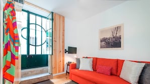 A room with a red sofa, a wooden door, and a black TV on a small table. - Cozy Apartment in Historical Lisbon by COZYSTAYS 1/5 (Lisbon)