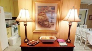 A dining area with a table set for two, two lamps, a framed landscape painting, and a buffet with various dishes. - It'll Do Two -  Private Pool Close to Beach (North Myrtle Beach)
