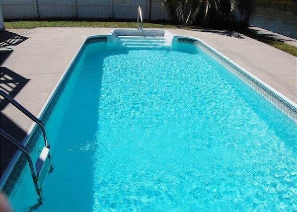 Une piscine rectangulaire à l’eau d’un bleu limpide, entourée d’une terrasse en béton.