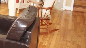 A living room with a brown leather sofa, a rocking chair, and a white chair with a red cushion. A wooden staircase is visible in the background. - It'll Do Two -  Private Pool Close to Beach (North Myrtle Beach)